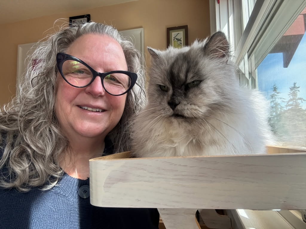 Phyllis smiling beside a fluffy gray rescue cat at a sunny window
