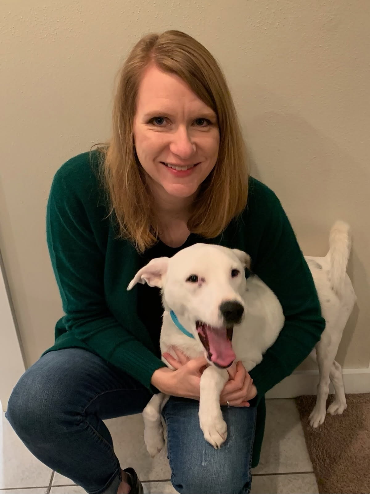 Sarah smiling while holding a happy white rescue puppy indoors