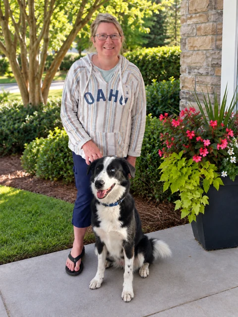 Bigi smiling with a black and white Border Collie mix on a sunny porch