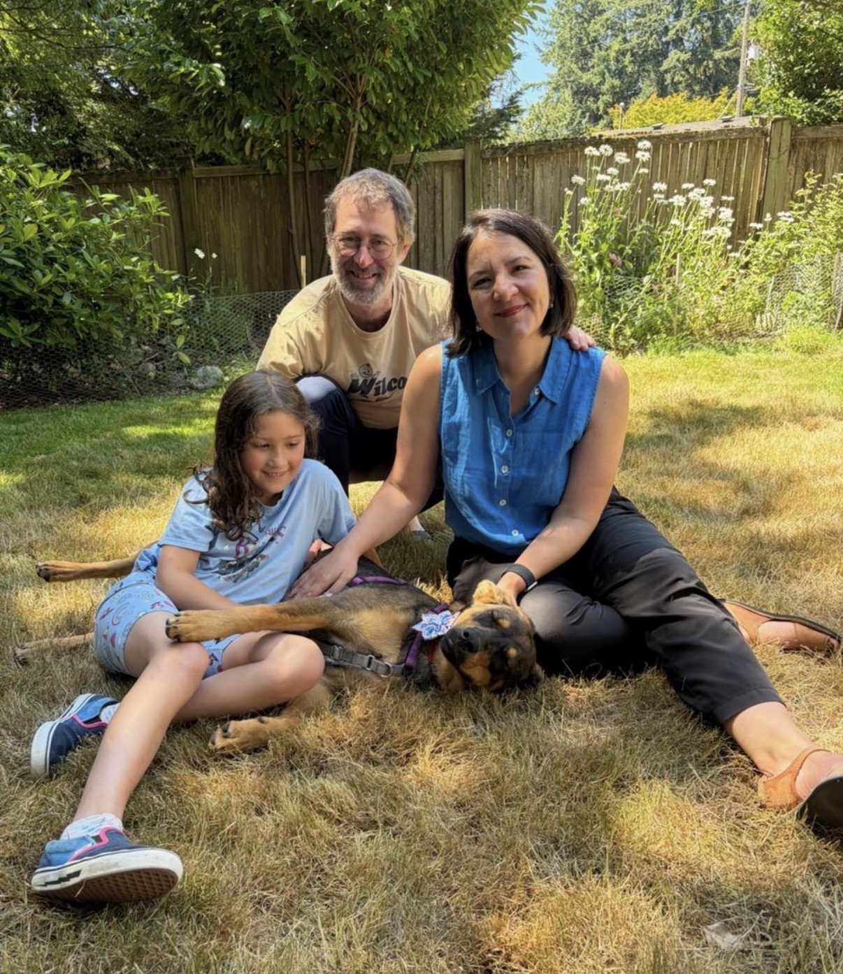 Family sitting in their sunny backyard with their newly adopted tan and black dog