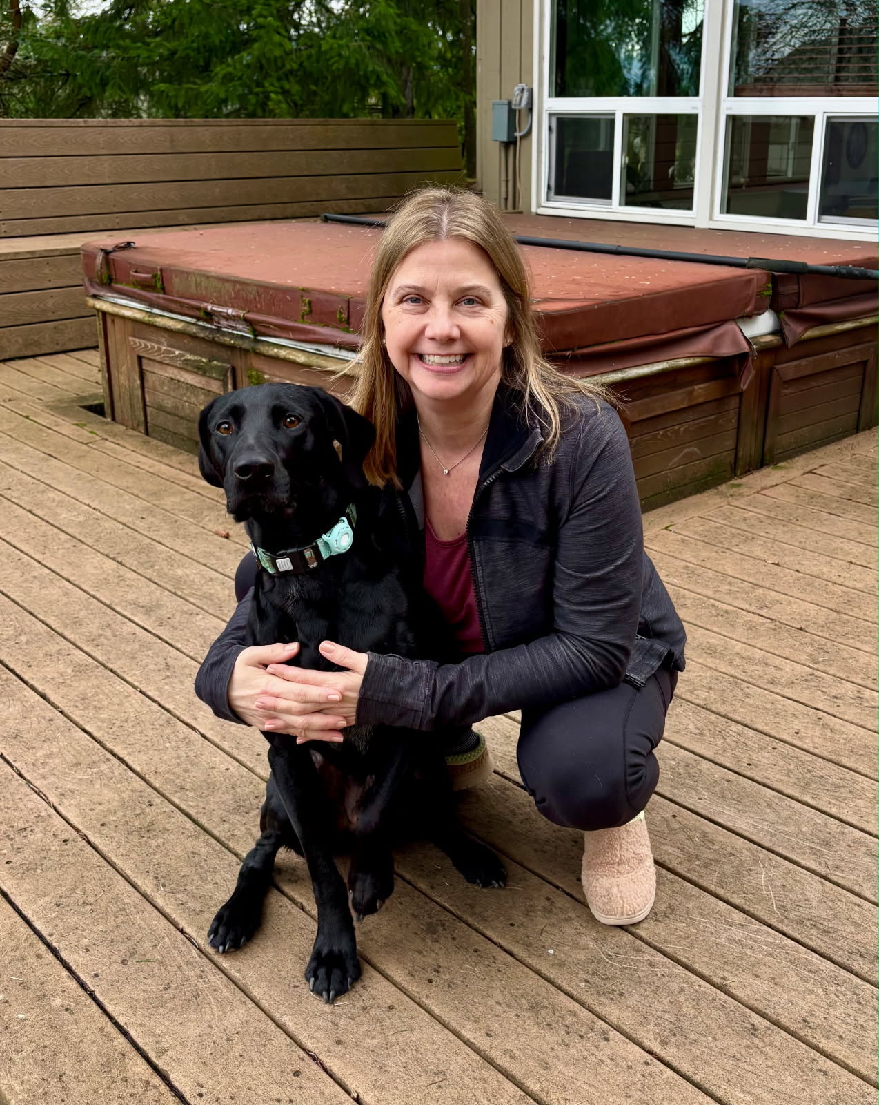 Jennifer kneeling beside a black rescue dog on a wooden deck