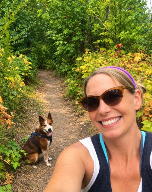 Jamie smiling on a wooded trail with a brown and white rescue dog